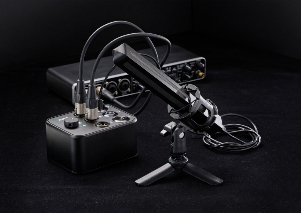 A black tabletop microphone on a tripod stand is connected by cables to an audio interface and a mixer, showcasing sleek Product Design NZ against a dark background.