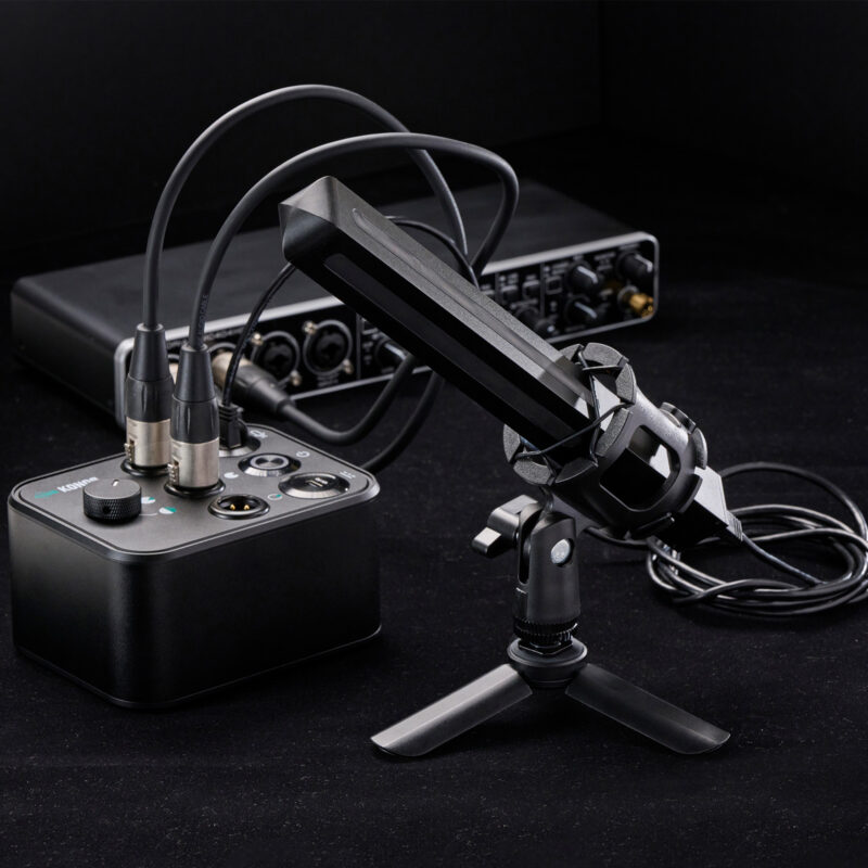 A black tabletop microphone on a tripod stand is connected by cables to an audio interface and a mixer, showcasing sleek Product Design NZ against a dark background.