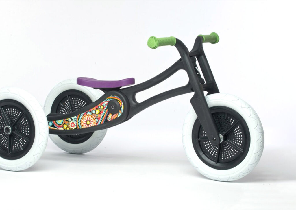 A colourful children's balance tricycle with a black frame, white tyres, green handlebars, purple seat, and vibrant decorative patterns on the body—an imaginative example of Product Design NZ—set against a plain white background.