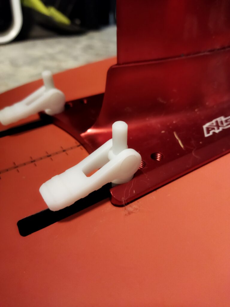 Close-up of a red board with white plastic fin clips and a fin box, showcasing clever Product Design NZ in the attachment mechanism, likely part of a surfboard or paddleboard.